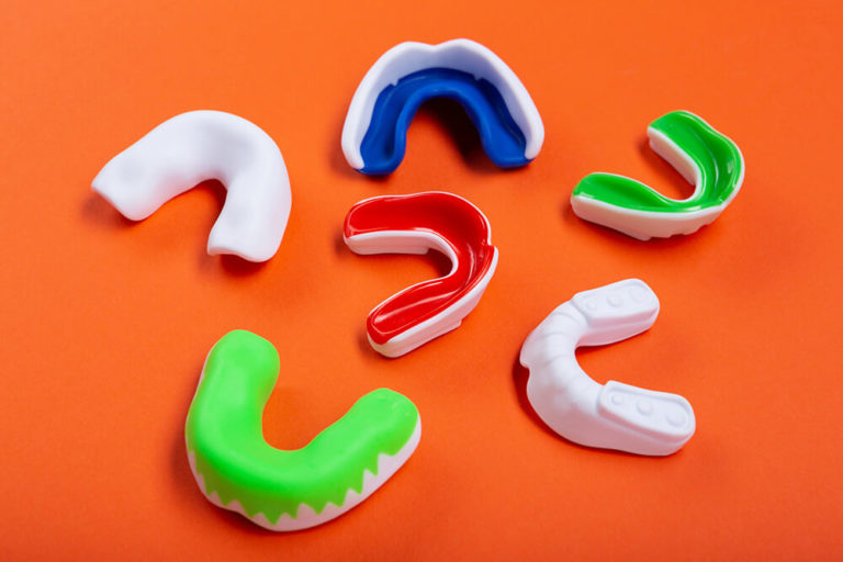 Six sports and teeth grinding mouth guards sitting on an orange background