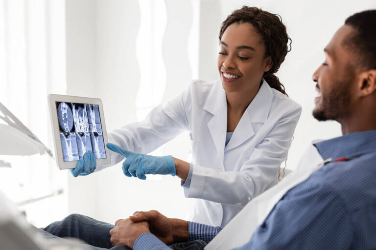 Dentist showing a patient dental X-rays on a tablet discussing the steps in a root canal, both smiling in a modern dental office.
