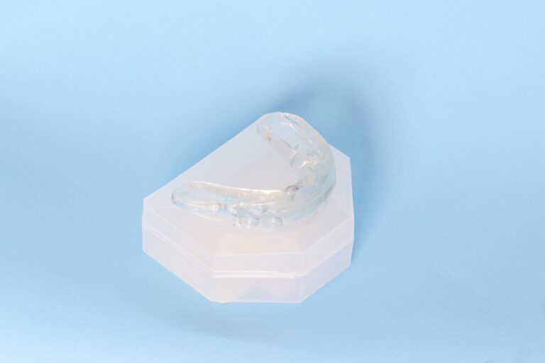 Clear dental night guard placed on a white storage case against a light blue background.