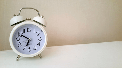 White analog alarm clock displaying the time 6:50, placed on a white surface.