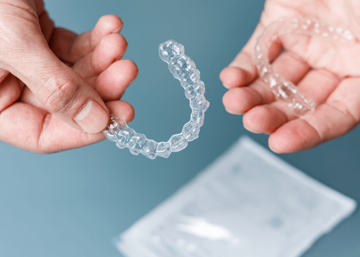Close-up of hands holding two clear dental aligners for orthodontic treatment.