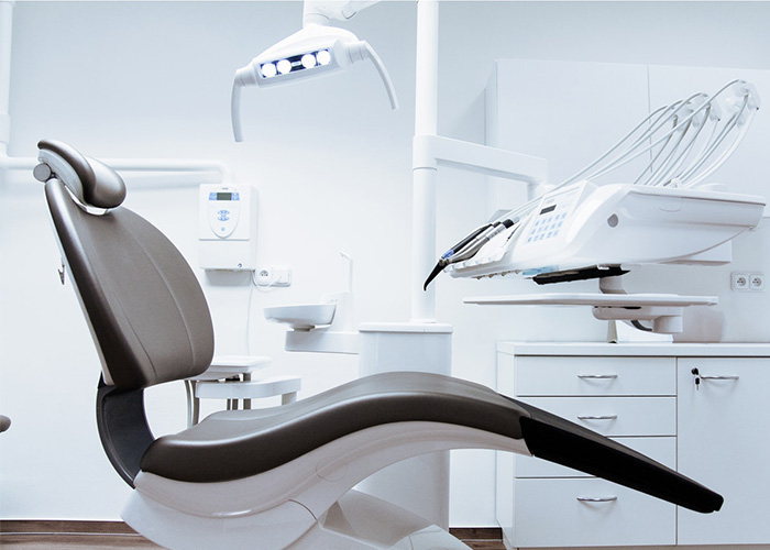 Empty modern dental chair in a clean and well-equipped dental office, with overhead light and dental tools.