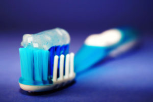 Close-up of a toothbrush with blue bristles and toothpaste on top against a dark blue background.