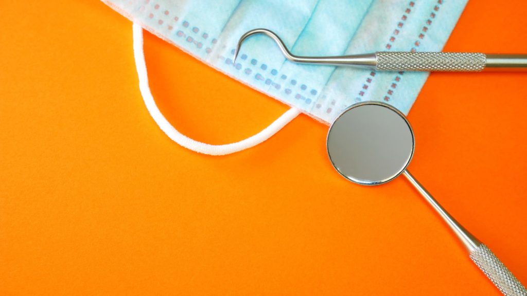 Dental checkup instruments with part of a surgical mask on an orange background