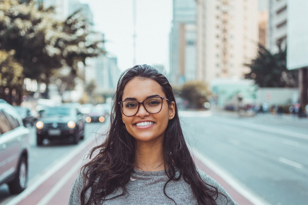 woman on busy street with glasses smiling at the camera with beautiful teeth