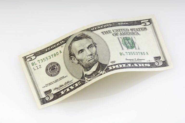 A five dollar bill on a gray background