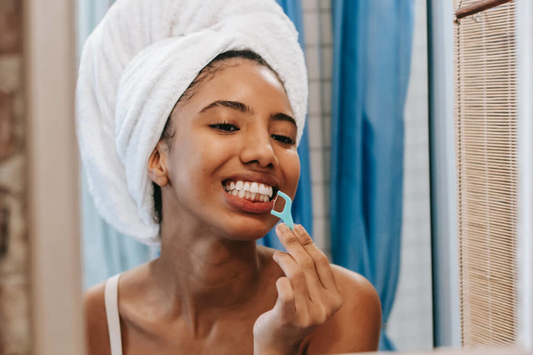 A woman looks in a mirror and uses a disposable flosser to floss her teeth including dental implants