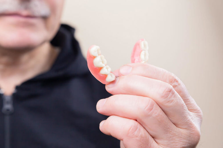 An out of focus man holds a pair of partial dentures