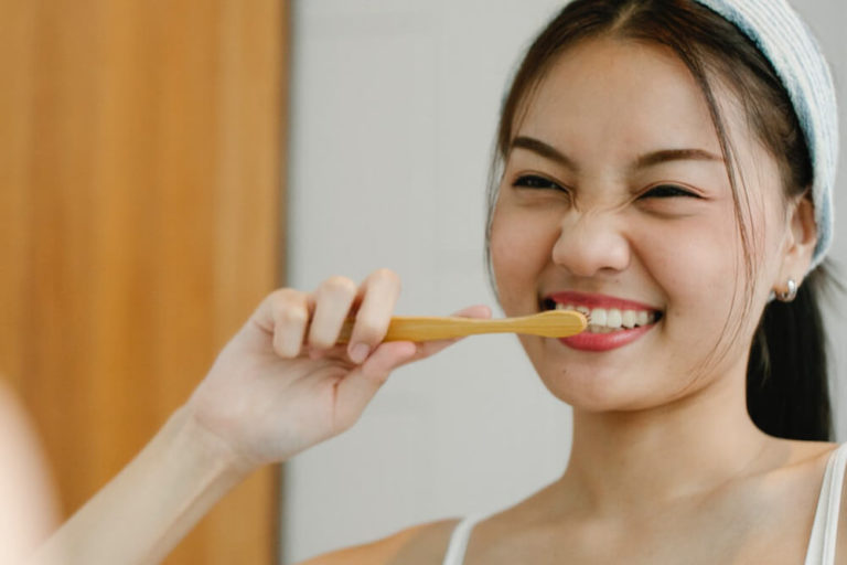 A woman looks in a mirror while brushing her sensitive teeth