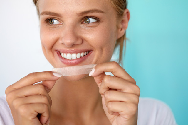 smiling woman holding a teeth whitening strip